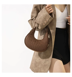 Détail du sac lune marron à motif crocodile avec boucle dorée sur un blazer kaki