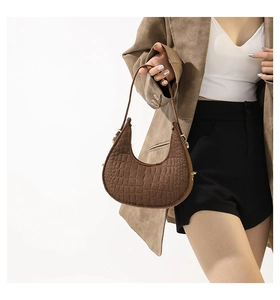 Détail de la texture cuir de crocodile marron foncé et finitions dorées sur le sac hobo