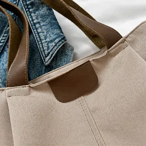 Primer plano detallado del bolso tote de lona con asa de cuero marrón y costuras