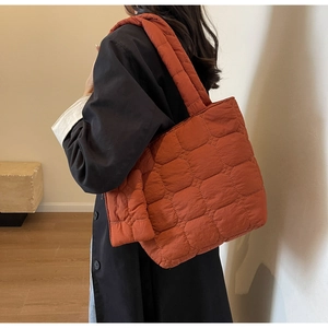 Detailed view of large quilted puffer tote bag with thick padded shoulder straps in brick red