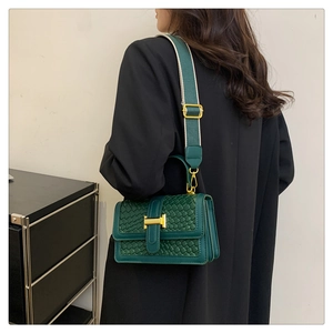 Détail du sac tissé vert avec boucle en H dorée et bandoulière large en toile