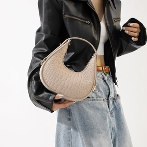 Sac sous le bras demi-lune beige avec gaufrage crocodile porté par un mannequin