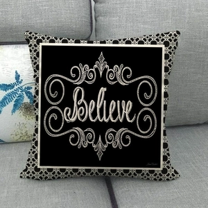 Detail of linen cushion cover with black letter print and white baroque scroll patterns