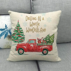Detalle de funda de cojín de lino con camión rojo y texto navideño en un sofá gris
