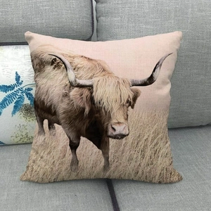 Close-up of linen pillow cover featuring a realistic highland cow print on a grey sofa