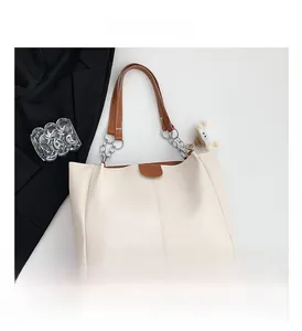 Detail of cream tote bag with brown leather strap, silver chain, and plush sheep charm