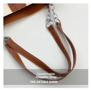 Close-up of brown leather shoulder strap with white stitching and silver metal chain links
