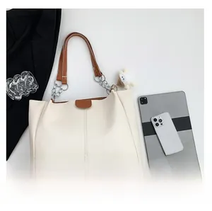 Cream tote bag with brown leather handles and a plush sheep pendant on a minimalist desk
