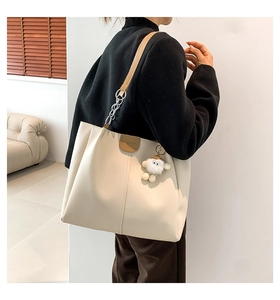 Detail of beige tote bag with brown leather straps and a cute white plush pendant