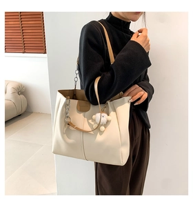 Detail of off-white leather tote bag with brown straps, metal chain, and plush pendant