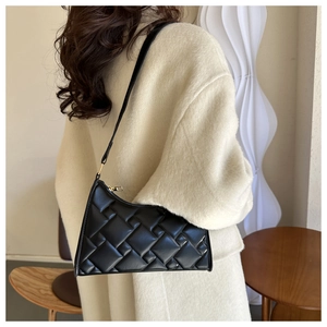 Detail of a black woven shoulder bag featuring a sleek asymmetric shape and golden zipper