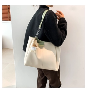 Detail of cream tote bag with green straps and fashion logo shown on model's shoulder