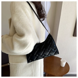 Detail of black woven shoulder bag styled with a white coat for a chic look