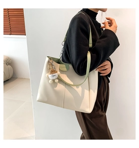 Detail of beige tote bag with green trim, fashion embossing and plush lamb charm accessory