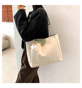 Chic beige tote bag with green trim and plush charm worn by model for daily commute