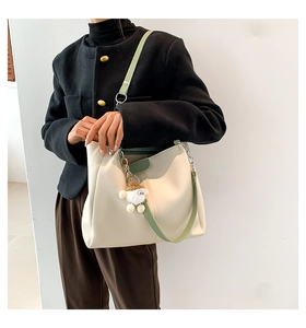 Beige leather tote bag with green straps and cute sheep pendant on model shoulder