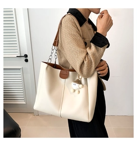 Detail of off-white tote bag with chain strap, leather trim, and plush charm accessory