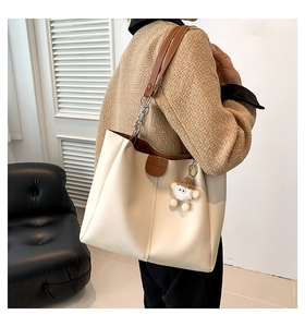 Off-white tote bag with brown chain strap and plush pendant shown on a model