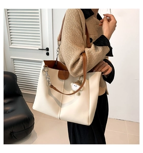 Detail of minimalist cream tote bag with brown trim, plush bear charm and fashion embossing