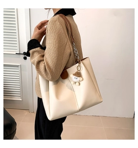 Detail of off-white tote bag with brown straps, silver chain and sheep charm accessory