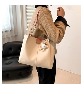 Detail of off-white tote bag with pink leather strap, chain, and plush charm