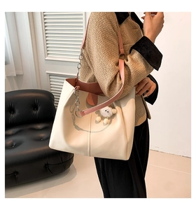 Detail of cream tote bag with pink leather strap, silver chain, and plush pompom charm