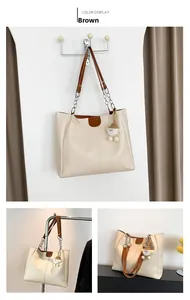 Detail of cream tote bag with brown trim, silver chain handle and plush charm accessory
