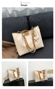 Detail of khaki tote bag featuring a decorative chain handle and white plush charm