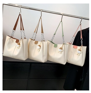Detail of four colorful tote bags with plush pendants and metal chain straps on display