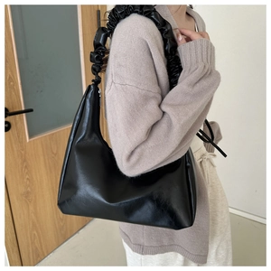 Macro shot of a black PU leather shoulder bag featuring a unique pleated cloud strap design
