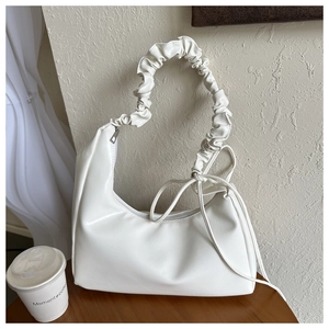 Detail of white minimalist shoulder bag featuring scrunchie handle and leather texture