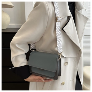 Detail of grey-blue square bag with geometric strap worn by model in trench coat