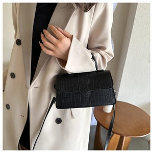 Dettaglio borsa a tracolla nera con stampa coccodrillo indossata con un blazer beige