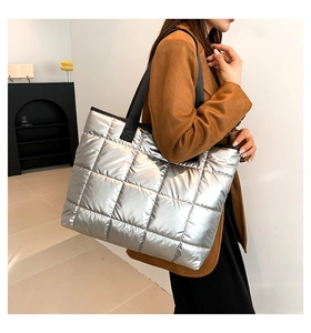 Detailed view of silver quilted tote bag with black wide straps on a model in brown coat