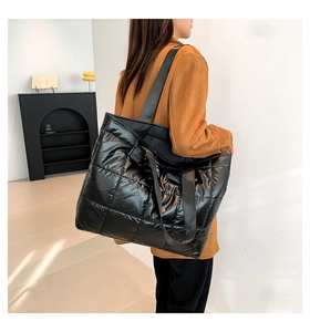 Detail of a large black quilted tote bag with soft padded texture and woven strap