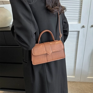 Borsa a mano marrone con motivo a coccodrillo indossata su un cappotto di lana nero