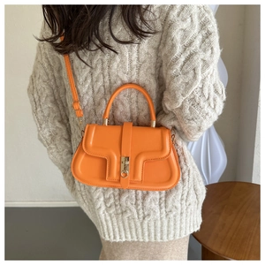 Detail of a bright orange saddle bag with gold ring buckle and textured faux leather finish
