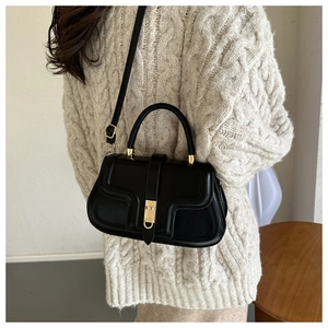 Chic black saddle bag with gold hardware worn over a cream knit sweater by a model
