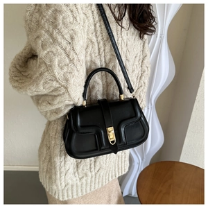 Close-up of minimalist black leather handbag with gold clasp on a beige knit sweater background