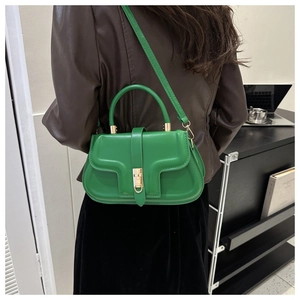 Detail of a green leather saddle bag worn crossbody with a minimalist metal lock closure
