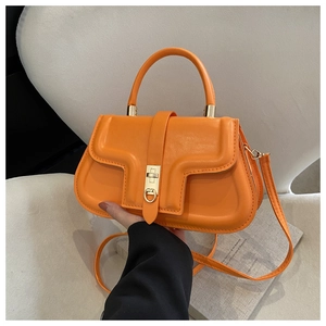 Detail of a bright orange crossbody saddle bag with gold metal lock and faux leather texture