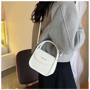 Detail shot of a white fashion crossbody bag worn by a model in a cozy cafe setting