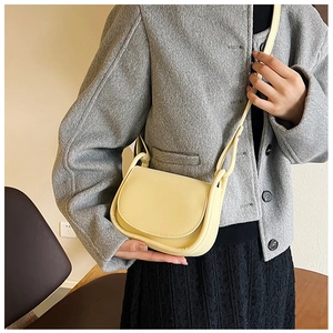 Détail d'un sac bandoulière jaune pâle porté sur un manteau gris au design de selle moderne