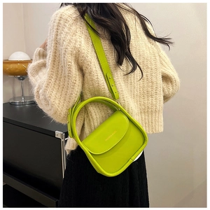 Detail showing bright green crossbody bag with gold fashion text and circular handle