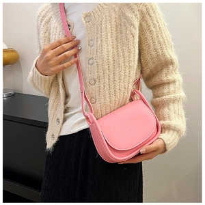 Détail d'un sac besace en cuir rose porté à l'épaule sur un pull beige avec sangle réglable