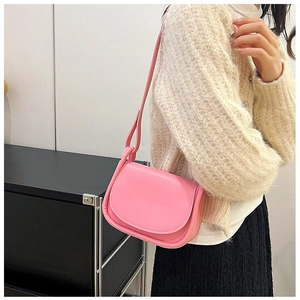 Modèle portant un sac selle rose minimaliste en cuir avec rabat et bandoulière épaule
