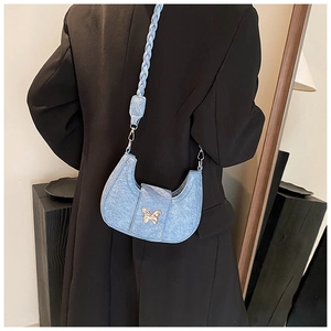Detail of light blue denim hobo bag featuring a golden butterfly clasp and woven shoulder strap