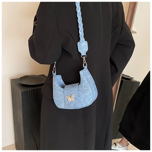Detail of light blue denim crescent hobo bag featuring a gold butterfly buckle and woven strap