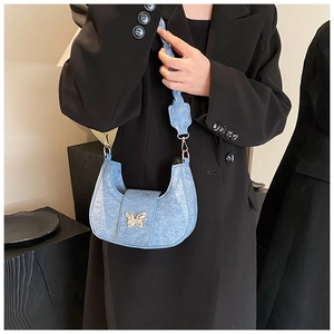 Detail of light blue denim crescent bag with golden butterfly buckle and woven strap