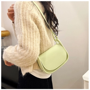 Gros plan d'un sac besace vert menthe porté sur un pull beige pour un style minimaliste